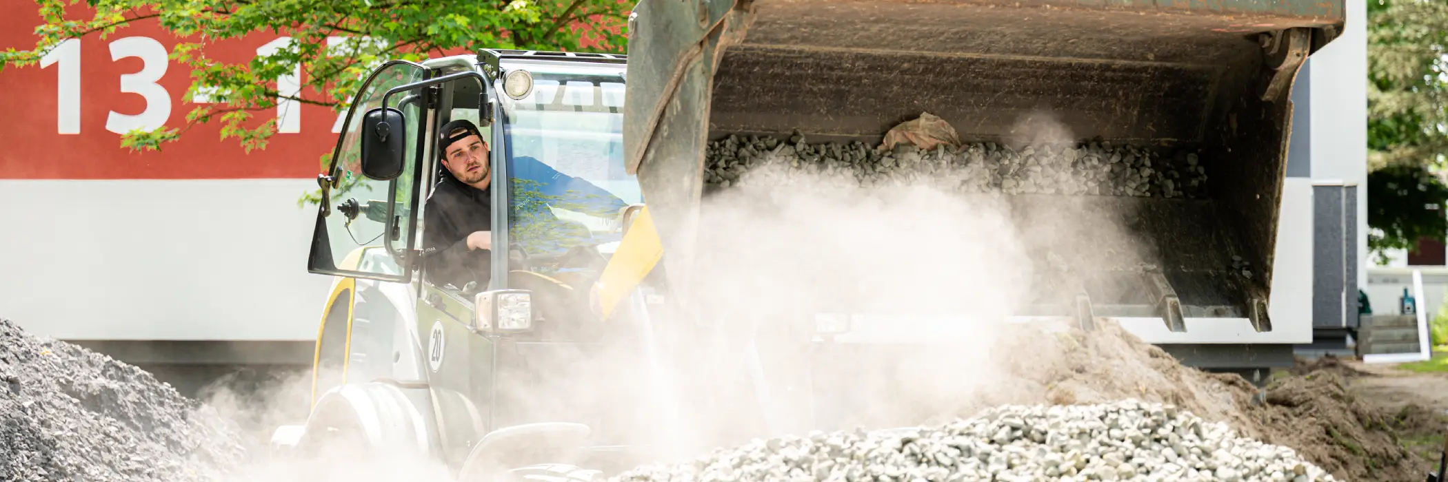 Frontlader kippt für Erdarbeiten Kieselsteine aus. Frontlader kippt für Erdarbeiten Kieselsteine aus.