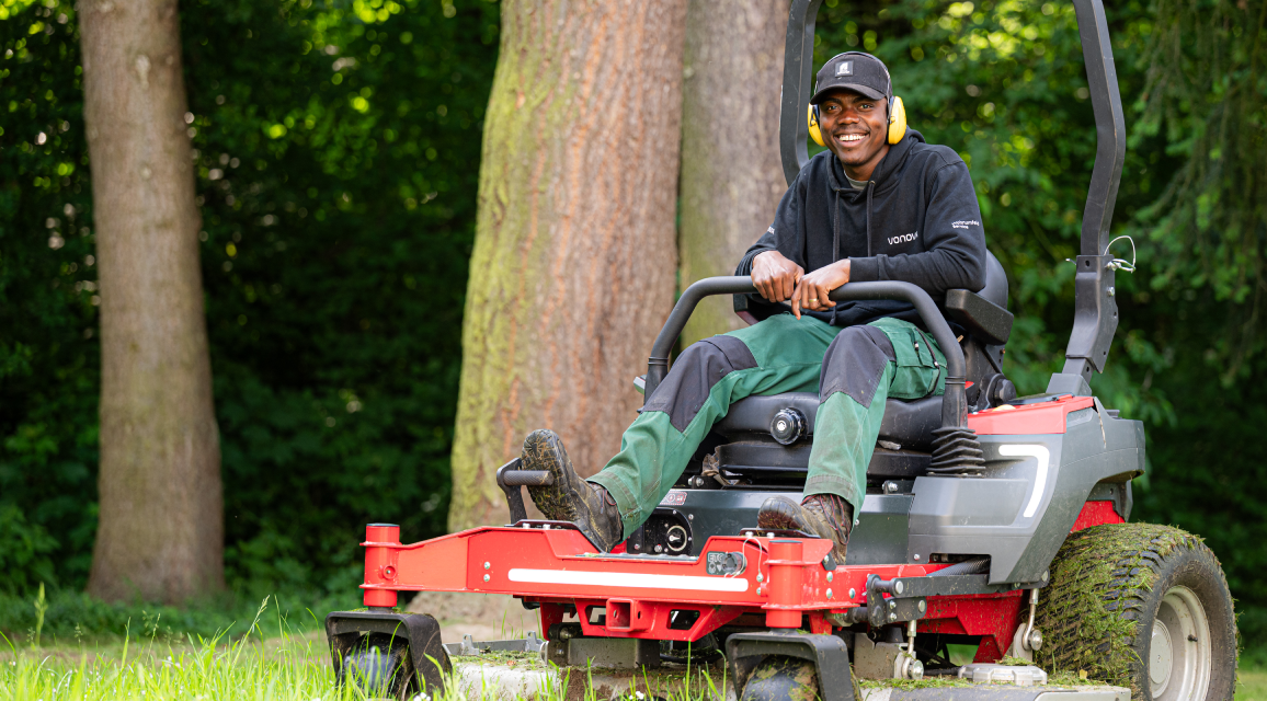 Mitarbeiter mit Hörschutz sitzt lächelnd auf seinem Arbeitsgerät. Mitarbeiter mit Hörschutz sitzt lächelnd auf seinem Arbeitsgerät.