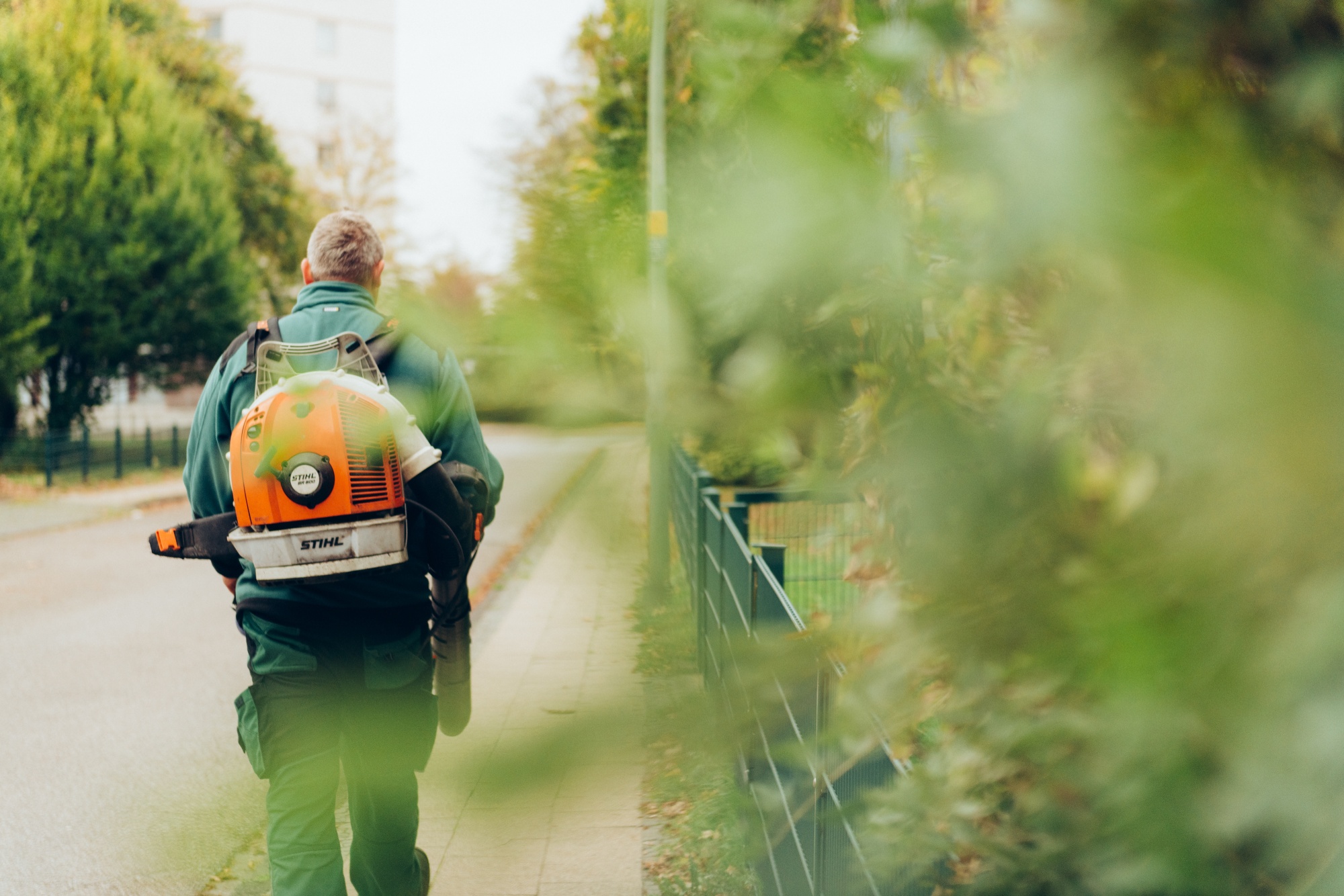 Mitarbeiter von hinten mit Laubbläser auf einer Straße bei der Außenanlagenpflege.