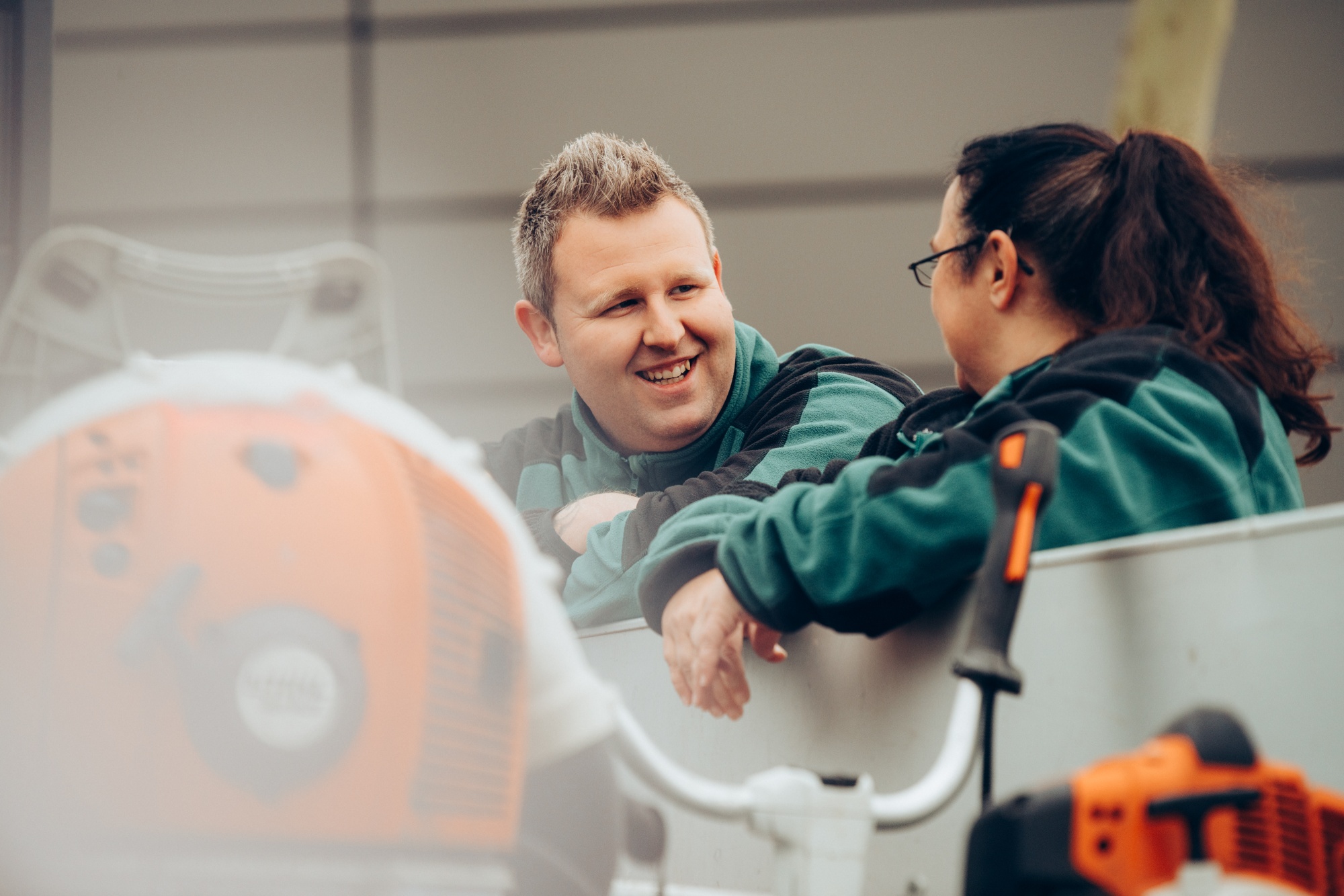 Vonovia Mitarbeitende des Grünflächen- und Gebäudeservices lachend im Gespräch über einen Transporter mit Werkzeugen gelehnt. Vonovia Mitarbeitende des Grünflächen- und Gebäudeservices lachend im Gespräch über einen Transporter mit Werkzeugen gelehnt.