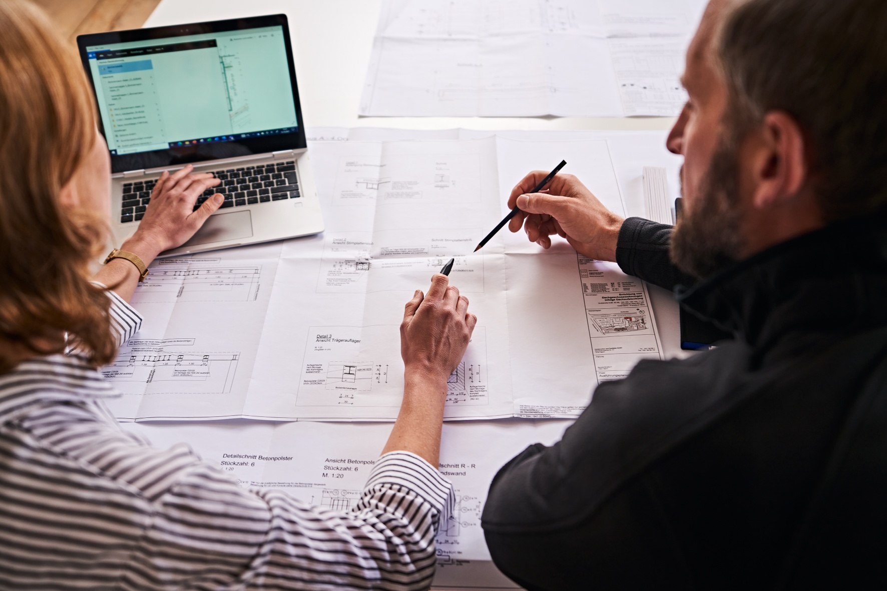 Zwei MItarbeitende von hinten vor einem Bauplan zur Freianlagenplanung. Zwei MItarbeitende von hinten vor einem Bauplan zur Freianlagenplanung.