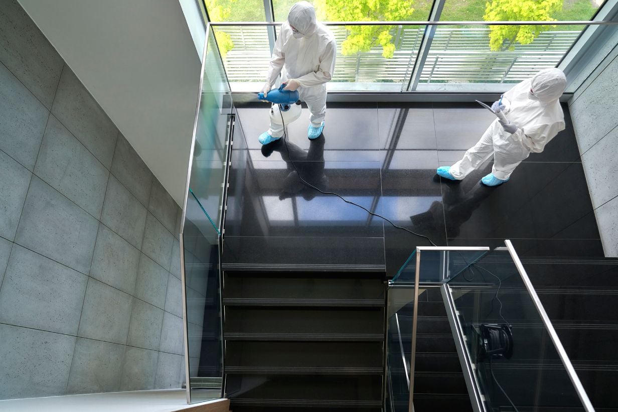Zwei Vonovia Mitarbeitende in Anzügen für die Spezialreinigung und Desinfektion eines Treppenhauses.